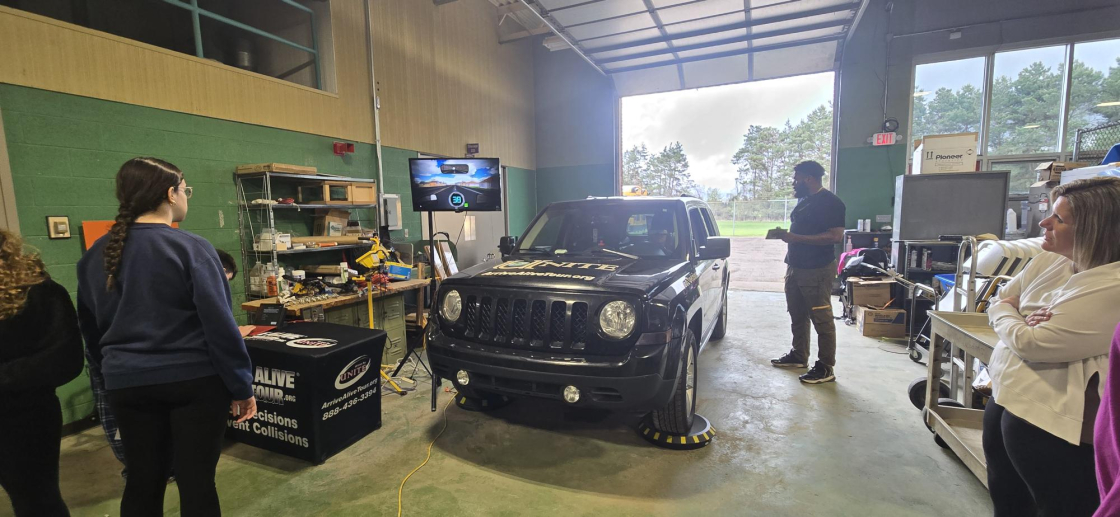 students standing in front of a car while a man talks