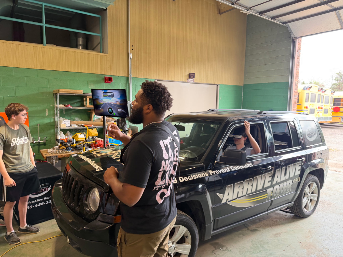 students standing in front of a car while a man talks
